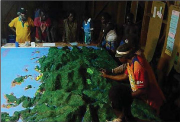 PHOTO: Boeboe community members add markers for local and traditonal ecological knowledge to the relief model of their village. Photo from J. X. Leon et al.(http://dx.doi.org/10.1080/08920753.2015.1046808)